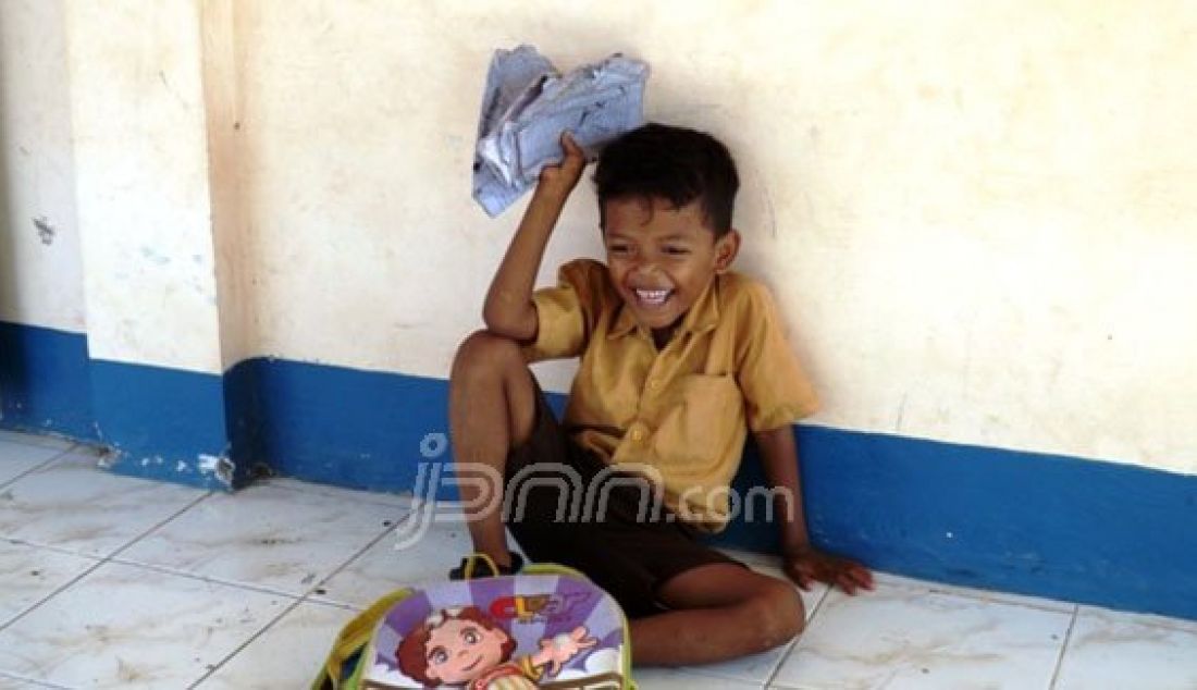 ISTIRAHAT: Seorang anak Sekolah Dasar (SD) di Gili Re, Jerowaru, Lombok Timur berusaha mengeringkan buku pelajaran yang basah terkena air laut saat menyebrang ke sekolahnya, Rabu (23/12). Foto: Wahyu/Lombok Pos/JPNN.com - JPNN.com