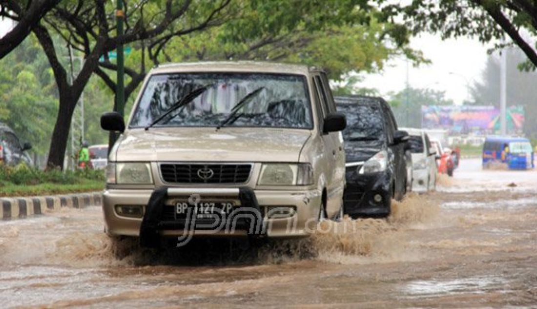 Sejumlah kendaraan berusaha menerobos genangan air hujan di Jalan Engku Putri, depan SPBU Regata,Batamcenter, Selasa (26/1). Genangan air hujan tersebut terjadi akibat tidak adanya saluran air di jalan tersebut. Foto: Cecep/Batam Pos/JPNN.com - JPNN.com