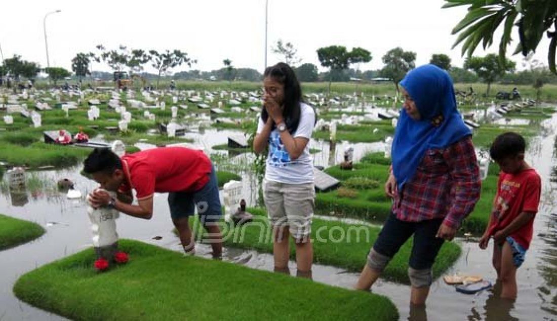 Salah satu keluarga berziarah di Tempat Pemakaman Umum Keputih Sukolilo yang tergenang banjir, Jumat (12/2). Foto: Satria/Radar Surabaya/JPNN.com - JPNN.com