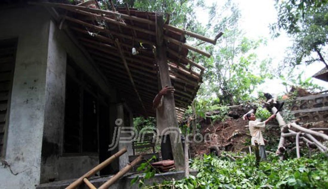 ROBOH: Seorang ibu pemilik rumah sedang memotong ranting-ranting pohon yang menimpa rumahnya, Selasa (16/2). Pohon tumbang ini diakibatkan oleh terjangan angin puting beliung. Foto: Okri/Radar Cirebon/JPNN.com - JPNN.com