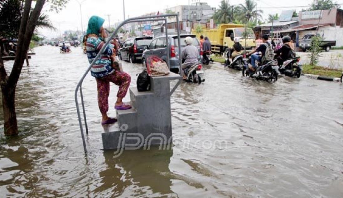 Seorang ibu denga balitanya berdiri di tengah kepungan banjir di jalan HR Soebrantas, Pekanbaru, Riau, Selasa (22/3). Hujan yang mengguyur kota Pekanbaru membuat jalan Hr Soebrantas terendam air dikarenaka tidak maksimal nya drainase. Foto: Akhwan/Riau Pos/JPNN.com - JPNN.com