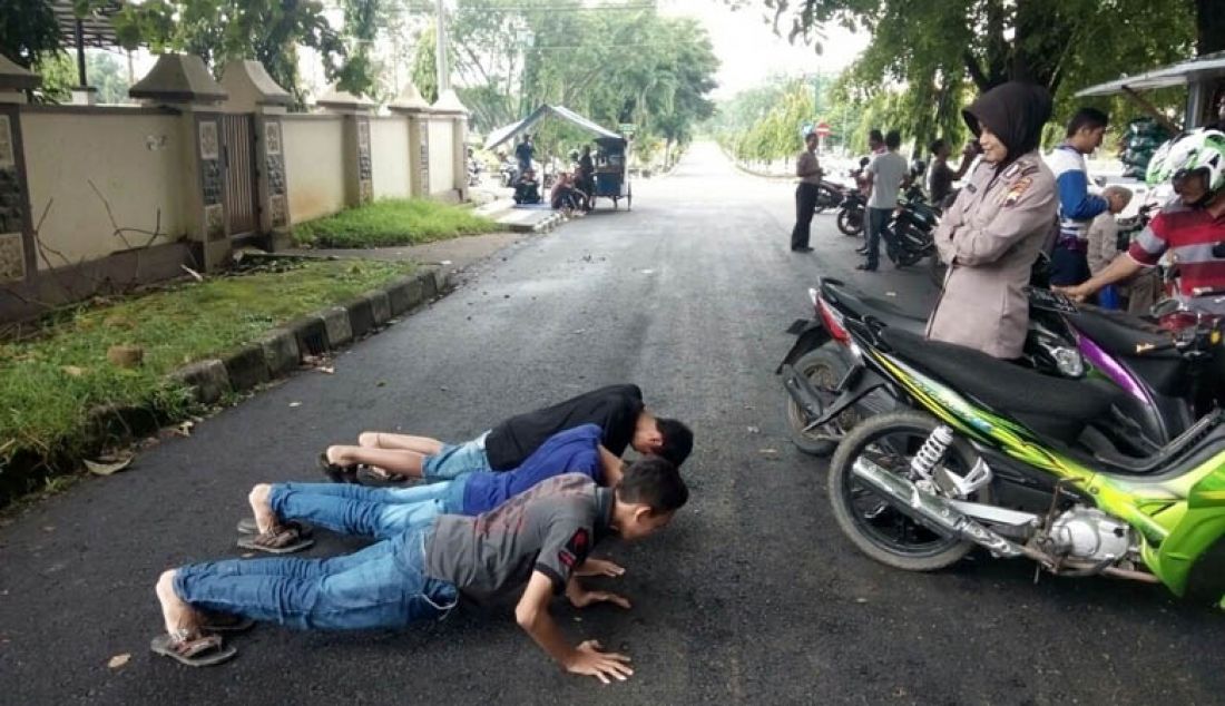 DISANKSI: Tiga bocah usia remaja tengah diberikan sanksi berupa Push Up lantaran diketahui mengendarai sepeda motor tanpa mengenakan helm. Foto: Triyono/Radar Pekalongan - JPNN.com