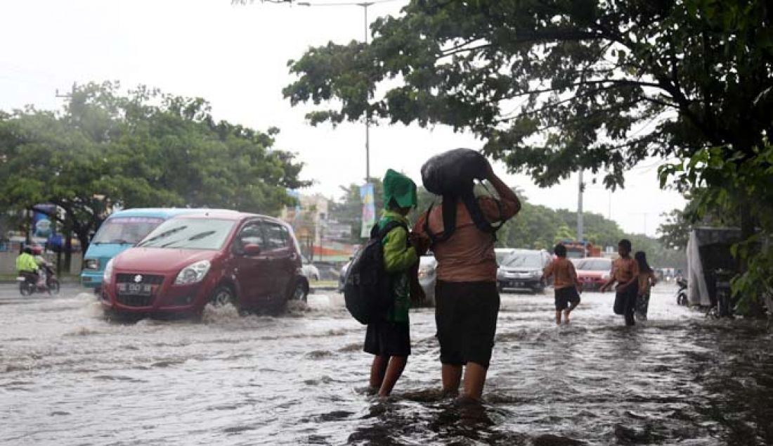 Murid Sekolah Dasar Negeri (SDN) Bontoramba Makassar berjalan di atas genangan air di Jalan Perintis Kemerdekaan, Makassar, Jumat (13/1). Tingginya genangan air di ruas jalan tersebut mengharuskan murid melepas sepatu saat pulang ke rumah. - JPNN.com