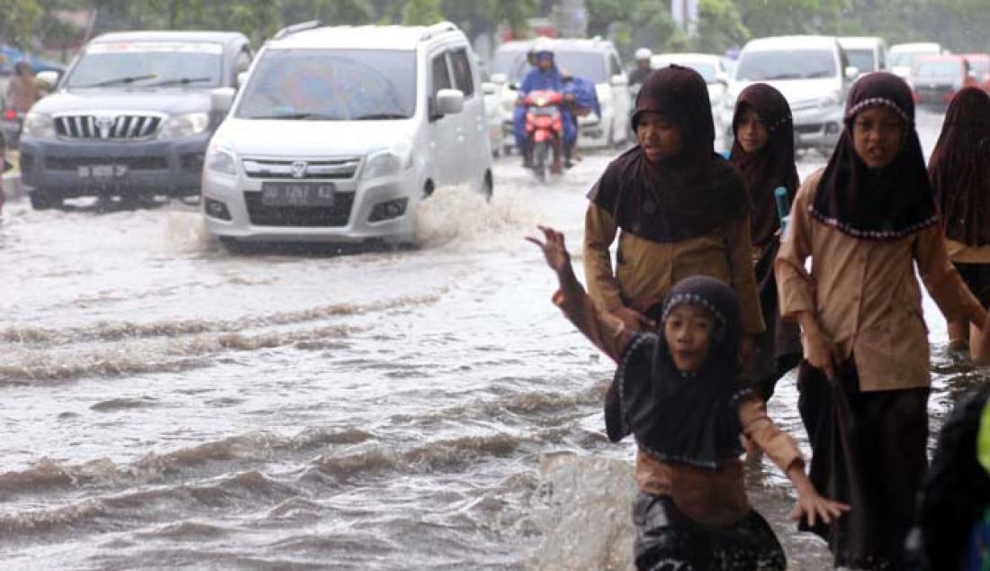 Murid Sekolah Dasar Negeri (SDN) Bontoramba Makassar berjalan di atas genangan air di Jalan Perintis Kemerdekaan, Makassar, Jumat (13/1). Tingginya genangan air di ruas jalan tersebut mengharuskan murid melepas sepatu saat pulang ke rumah. - JPNN.com