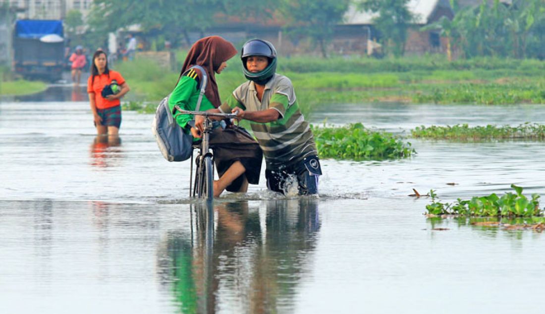 Seorang pria berjalan menerobos genangan banjir untuk mengantarkan putrinya berangkat sekolah di Dusun Kedungringintengah, Desa Kedungringin, Beji, Pasuruan, Jumat (13/1). Banjir kiriman membuat sejumlah warga dusun sekitar mengungsi dari tempat tinggalnya yang terendam banjir. - JPNN.com