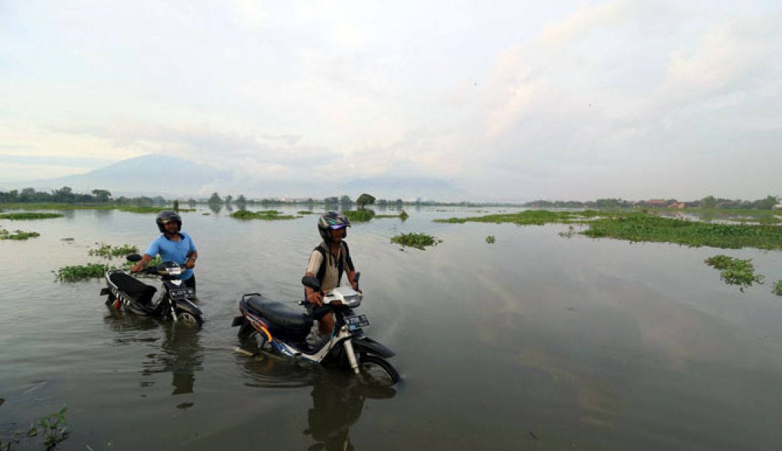 Dua warga melintas sambil menuntun motornya yang terendam banjir di jalan Dusun Kedungringintengah, Desa Kedungringin, Beji, Pasuruan, Jumat (13/1). Banjir kiriman membuat sejumlah warga dusun sekitar mengungsi dari tempat tinggalnya yang terendam banjir. - JPNN.com