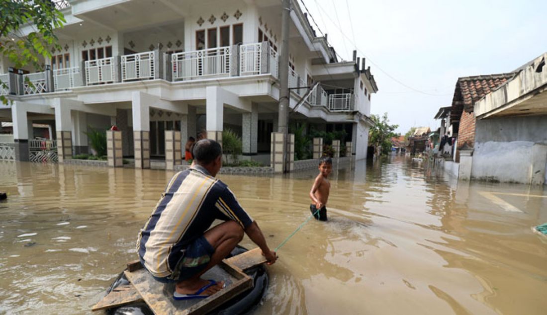 Tak ingin ayahnya berbasah-basah, Riyan akhirnya menuntunnya dengan ban bekas menuju rumahnya di Dusun Kedungringin tengah, Desa Kedungringin, Beji, Pasuruan, Jumat (13/1). Banjir kiriman yang merendam kampung ini membuat warga dusun setempat sebagian memilih mengungsi. - JPNN.com