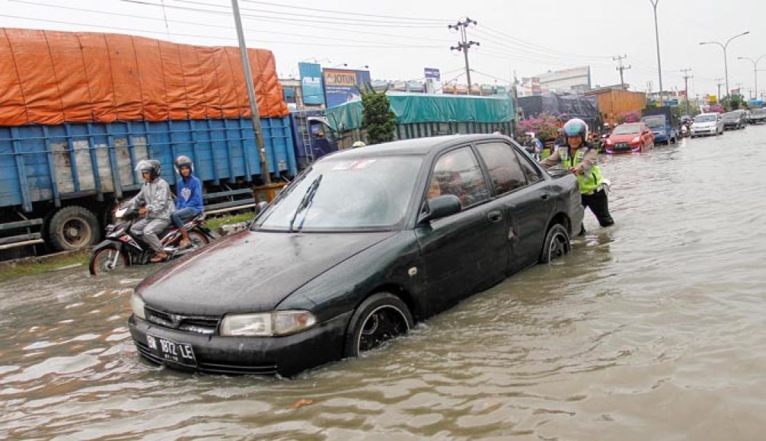 DORONG: Petugas Lantas Polsek Tampan Aiptu Dedi S mendorong kendaraan yang mogok saat melewati genangan air di Jalan Hr Soebrantas. Pekanbaru. Riau Selasa (31/1/2017) Hujan deras pada selasa pagi membuat Jalan Hr Soebrantas tergenang air hingga sebabkan kemacetan. - JPNN.com