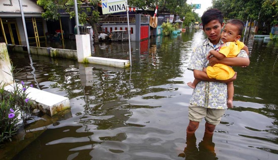 Ari Pratama (15) tampak menggendong adiknya Prama Andika 3 melintas di jalan Kupang Kidul kecamatan Jabon, Sidoarjo, Kamis (2/2). Genangan banjir tak kunjung surut hampir satu bulan menggenangi rumah mereka hingga selutut orang dewasa. - JPNN.com