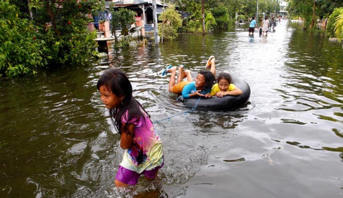 Abelia Nudiastuti tampak menarik dua temannya Dila Febrianan dan Aprilia Pujiastuti di genangan banjir dengan menggunakan ban di Jalan Kupang Kidul kecamatan Jabon, Sidoarjo, Kamis (2/2). Genangan banjir tak kunjung surut hampir satu bulan menggenangi rumah mereka hingga selutut orang dewasa. - JPNN.com