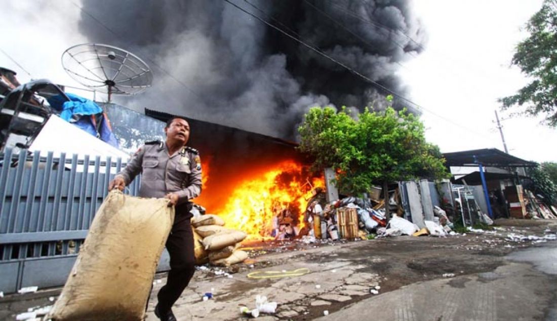 Seorang Polisi mengevakuasi barang dari gudang daur ulang plastik Lawang, Kabupaten Malang, Jawa Timur, yang terbakar hebat, selasa (08/02). Akibat kejadian tersebut ditaksir mengalami kerugian Rp 10 Miliar. - JPNN.com