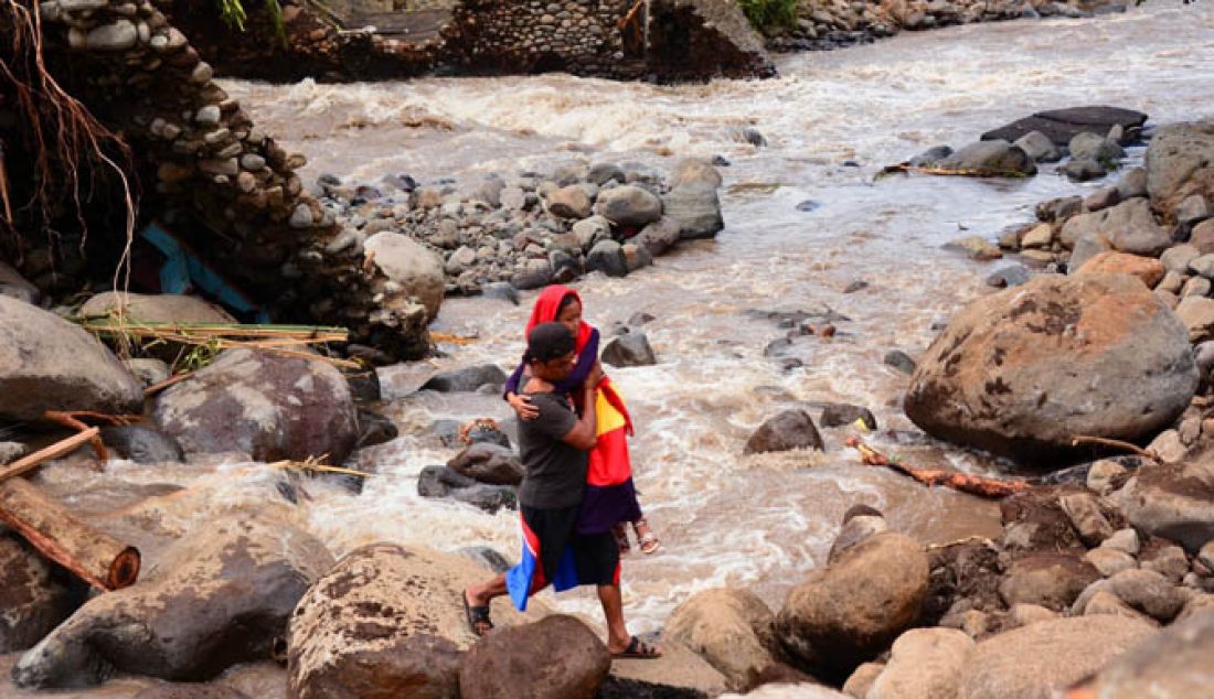 TERISOLIR: Sahnun, salah seorang warga Sambaelia, Lombok Timur menggendong anaknya untuk menyeberangi sungai, Sabtu (11/2). Warga Dusun Kokok Raja Sambelia ini menjadi korban banjir bandang dan terisolir karena akses jambatan terputus. - JPNN.com