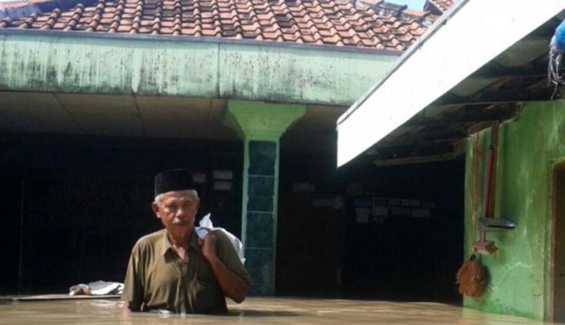 TERGENANG: Seorang warga keluar dari rumahnya yang terendam di Desa Limbangan, Brebes, Jumat (17/2). Bencana banjir bandang yang terjadi di wilayah Kecamatan Brebes dan Wanasari mulai surut, Jumat (17/2) siang. Hal itu setelah debit Sungai Pemali mulai menyusut. - JPNN.com