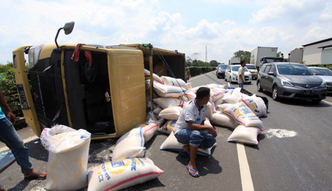 Paiton, Sopir Truk B 9271 NDC duduk diatas beras yang tumpah ke jalan akibat kendaraannya terbalik di Jalan Tol Tangerang-Merak km 53, Minggu (5/3). Truk terbalik karena pengalami pecah ban pada roda belakang. - JPNN.com