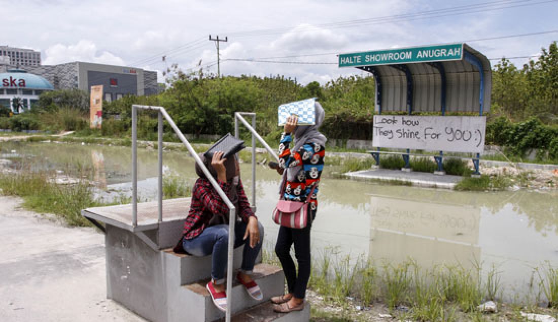 Pengguna jasa angkutan transportasi umum menutup kepalanya dari panas teriknya matahari saat menunggu kedatangan Bus TMP di Halte Portable yang terendam air di Jalan Soekarno-Hatta Pekanbaru, Selasa (7/3). - JPNN.com