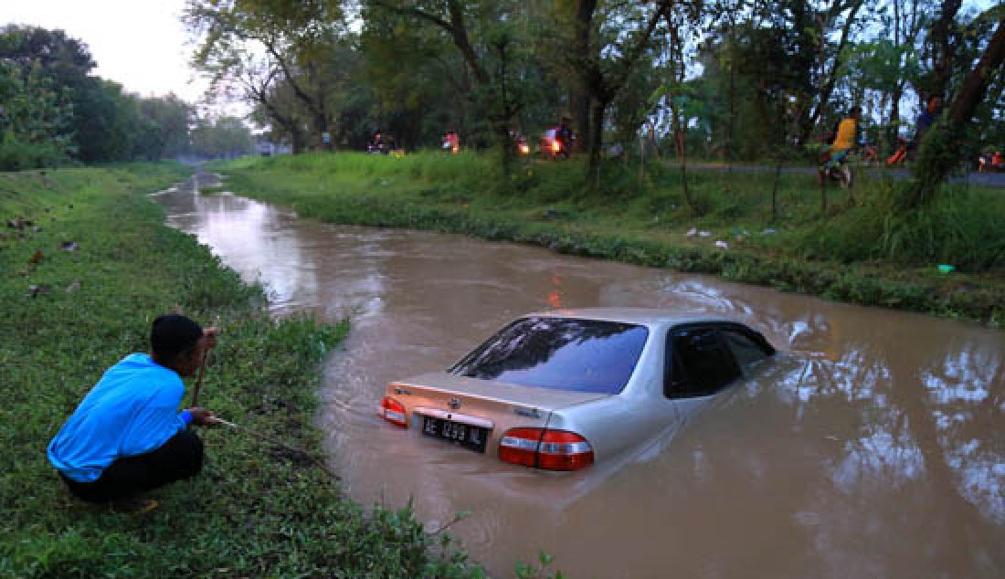 Sebuah mobil sedan bernopol AE 1299 NL yang mengalami pecah ban sebelah kiri lalu terpelanting menabrak pohon dan terjun ke kanal Jiwan, Desa Teguhan, Kecamatan Jiwan, kab. Madiun, Kamis (9/3). - JPNN.com