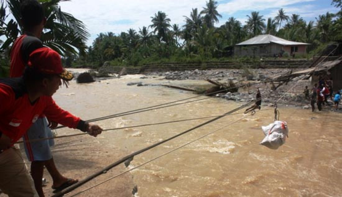 Tim CSR PT Semen Padang dan Dinas sosial sedang membantu logistik melewati sungai dekat jembatan yang putus akibat banjir bandang, Minggu (12/3). Putusnya jembatan gantung Baringin, Kecamatan Lubukkilangan akibat diterjang banjir bandang itu membuat ribuan warga terisolasi. - JPNN.com