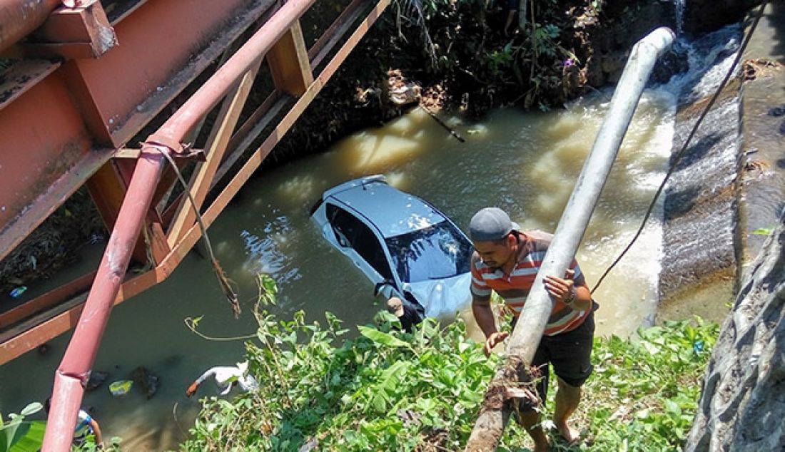 SINGKIRKAN PIPA: Seorang warga membantu menyingkirkan pipa di bawah jembatan untuk memperlancar proses evakuasi mobil dari dalam sungai, Rabu (23/5). Kecelakaan tersebut diduga karena pengemudi mengantuk sehingga tidak dapat mengendalikan kendaraan. - JPNN.com