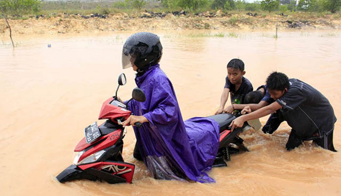 nak-anak mendorong motor yang mogok di Jalan Marinacity, Tanjunguncang, Batuaji, JUmat (26/5). Hujan deras yang mengguyur Batam membuat sebagian wilayah Batam banjir. - JPNN.com