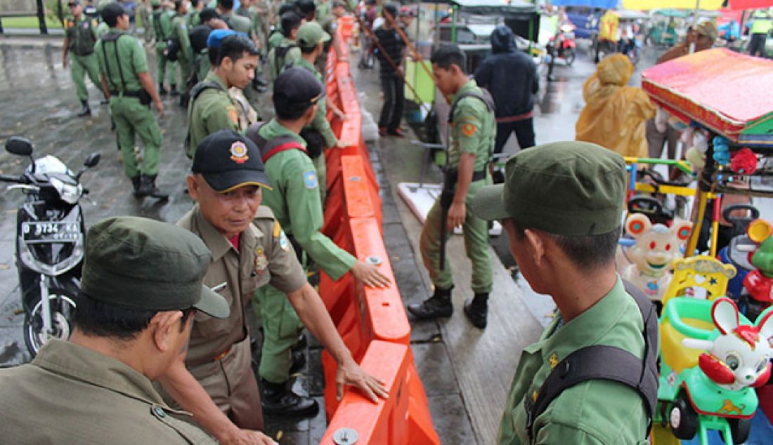 STERILKAN: Anggota Pol PP dan Linmas Kota Tasikmalaya memasang penyekat di kawasan Taman Kota Tasikmalaya depan Masjid Agung Minggu (28/5). Penyekatan itu untuk menyeterilkan Taman Kota dari Pedagang Kaki Lima (PKL) dan tukang penyewaan mainan. - JPNN.com