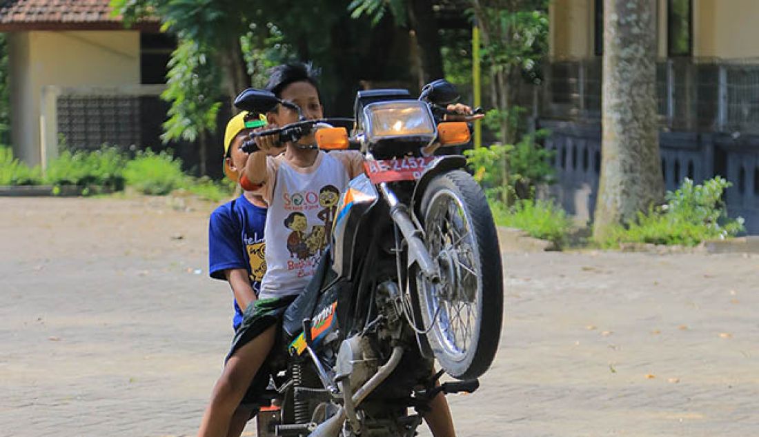 ua orang remaja melakukan wheelie dengan menggunakan motor dinas di halaman museum Trinil kabupaten Ngawi, Senin (30/5). Museum Trinil menjadi jujugan warga sekitar Ngawi untuk menunggu waktu berbuka puasa selama bulan ramadhan. - JPNN.com