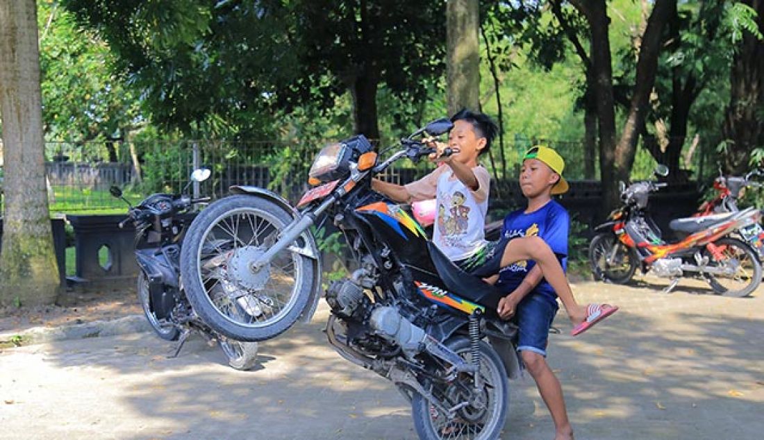 ua orang remaja melakukan wheelie dengan menggunakan motor dinas di halaman museum Trinil kabupaten Ngawi, Senin (30/5). Museum Trinil menjadi jujugan warga sekitar Ngawi untuk menunggu waktu berbuka puasa selama bulan ramadhan. - JPNN.com