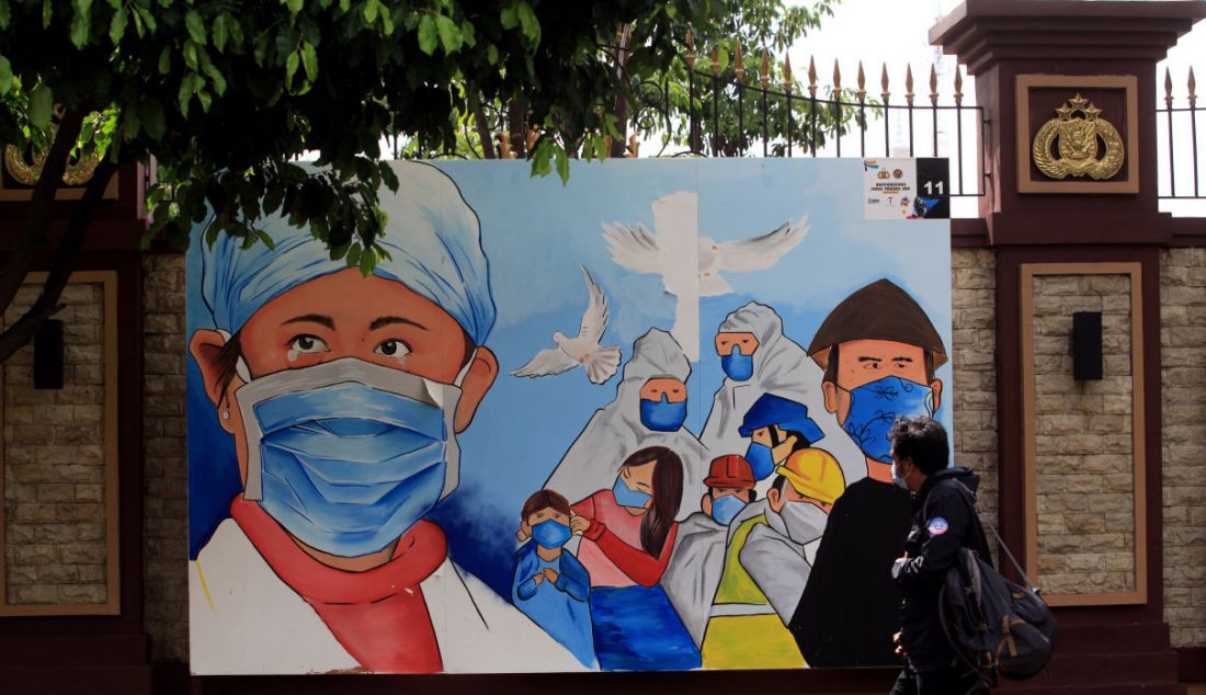 Warga melintas di depan mural di Lapangan Bola Mabes Polri, Jakarta, Selasa (23/11). Mural berisi imbauan waspada Covid-19. - JPNN.com