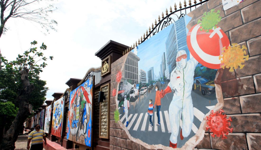 Warga melintas di depan mural di Lapangan Bola Mabes Polri, Jakarta, Selasa (23/11). Mural berisi kritikan terhadap institusi kepolisian dan imbauan waspada Covid-19. - JPNN.com