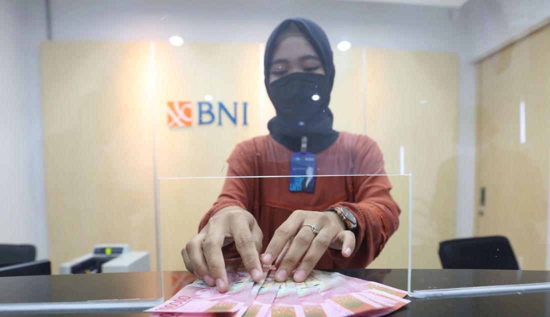 Pegawai BNI saat menerima uang di salah satu kantor cabang PT Bank Negara Indonesia (Persero) Tbk. di Sentul, Kabupaten Bogor, Jawa Barat, Jumat (17/12). Berdasarkan data BNI nilai transaksi aplikasi mobile BNI mencapai Rp 160 triliun hingga kuartal III/2021, sementara nilai transaksi anjungan tunai mandiri (ATM) turun ke angka Rp 137 triliun. - JPNN.com