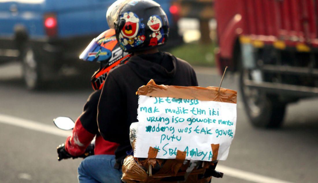 Pemudik sepeda motor menempelkan kertas berisi tulisan di bagian belakang motor saat melintasi jalur mudik Simpang Jomin, Karawang, Jawa Barat, Jumat (29/4). Tulisan tersebut berupa curhat mereka mengenai mudik. - JPNN.com