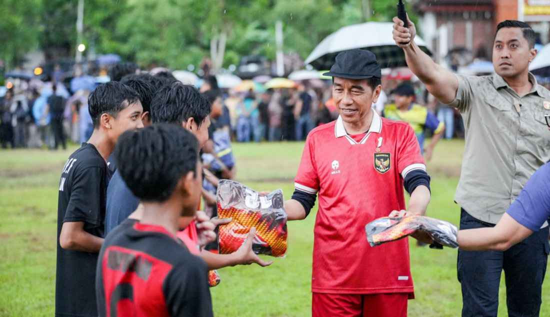 Presiden Jokowi membagikan kaus kepada anak-anak seusai main bola di Lapangan Gamplong, Moyudan, Sleman, Sabtu (27/1). Jokowi bermain sebagai penjaga gawang di bawah guyuran hujan deras. - JPNN.com