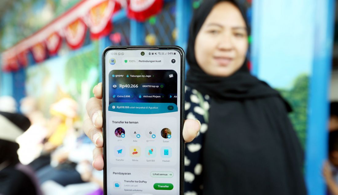 Orang tua murid menunjukkan saldo GoPay seusai anaknya menukarkan koin menjadi saldo digital pada mesin penukaran di TK Darma Bakti, Kota Depok, Jawa Barat, Jumat (9/8). Kegiatan yang dilaksanakan GoPay dengan menggandeng Koinan.id dalam mengkonversi koin Rupiah menjadi saldo GoPay secara otomatis tersebut sebagai upaya mendukung pemerintah dalam mendorong transaksi nontunai serta mengatasi masalah uang koin bagi kemajuan UMKM. - JPNN.com