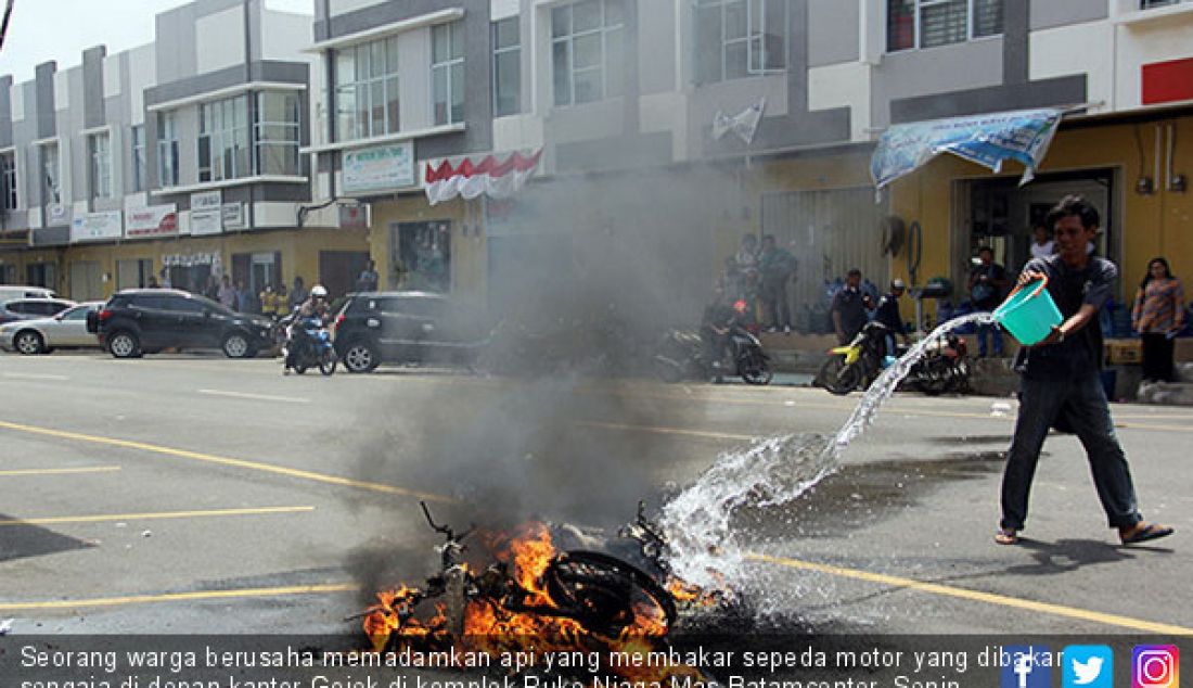 Seorang warga berusaha memadamkan api yang membakar sepeda motor yang dibakar sengaja di depan kantor Gojek di komplek Ruko Niaga Mas Batamcenter, Senin (16/10). Pembakaran sebagai bentuk protes terhadap ojek online. - JPNN.com