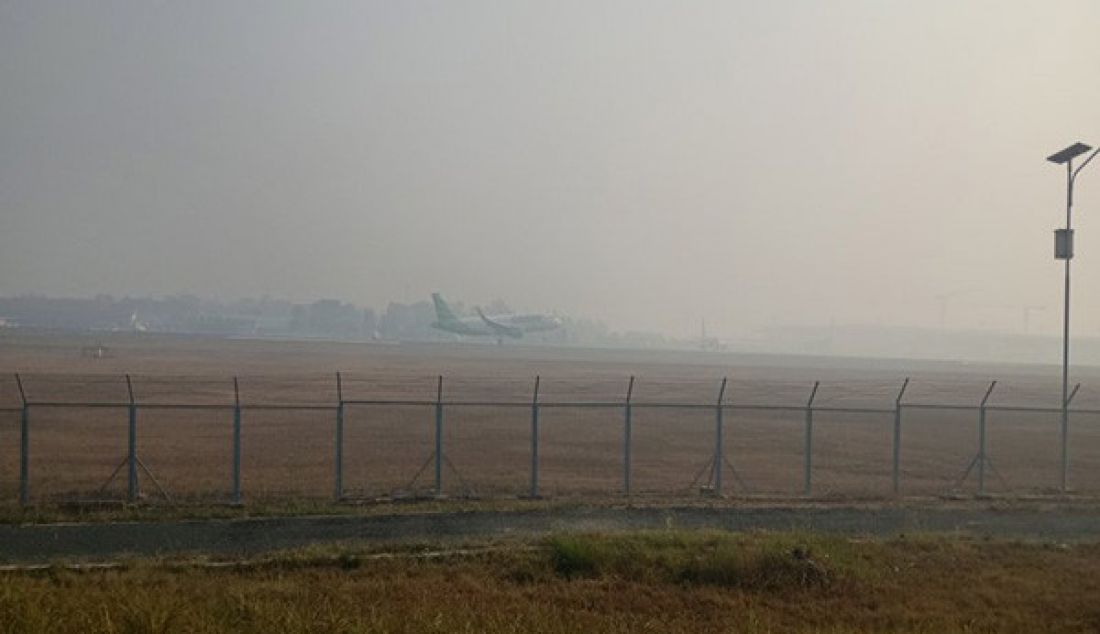 Sebuah pesawat yang landing di Bandara Syamsudin Noor di tengah landasan pacu tertutup asap. Sejumlah penerbangan pun turut terganggu akibat kabut asap. - JPNN.com