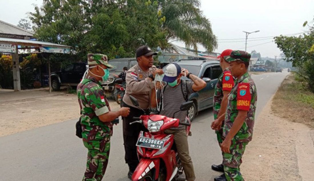 Anggota TNI dan Polri membagikan masker kepada pengendara motor yang melewati perbatasan Jagoi Babang. - JPNN.com