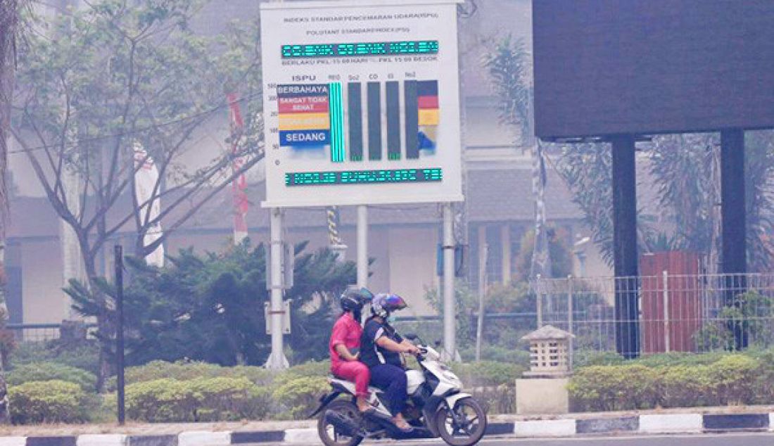 Pengendara motor melintasi layar monitor ISPU yang menunjukkan PM 10 berada di angka 500 sehingga udara di Kota Palangka Raya berbahaya. - JPNN.com