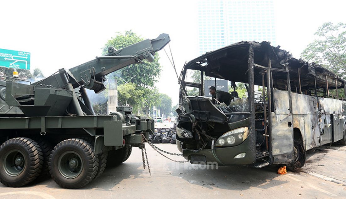 Petugas saat mengevakuasi bangkai bus milik TNI yang dibakar massa pasca bentrok antara mahasiswa dengan petugas keamanan di Lapangan Tembak, Jakarta, Rabu (25/9). - JPNN.com