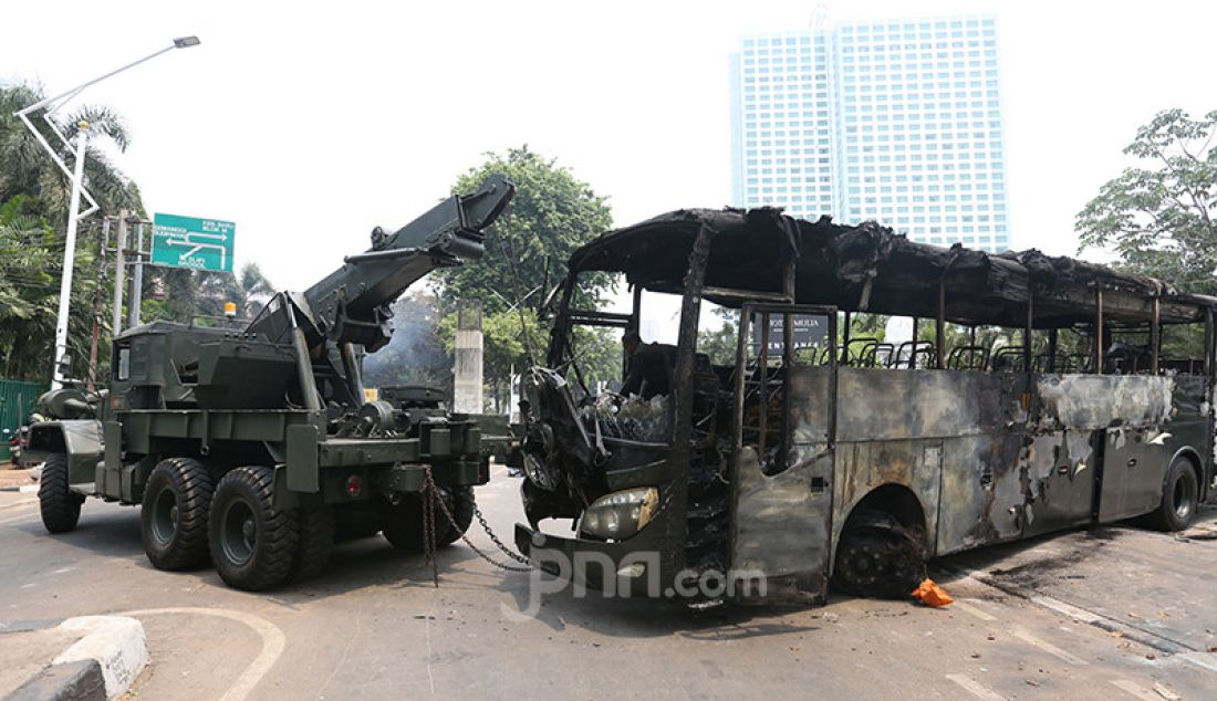 Petugas saat mengevakuasi bangkai bus milik TNI yang dibakar massa pasca bentrok antara mahasiswa dengan petugas keamanan di Lapangan Tembak, Jakarta, Rabu (25/9). - JPNN.com