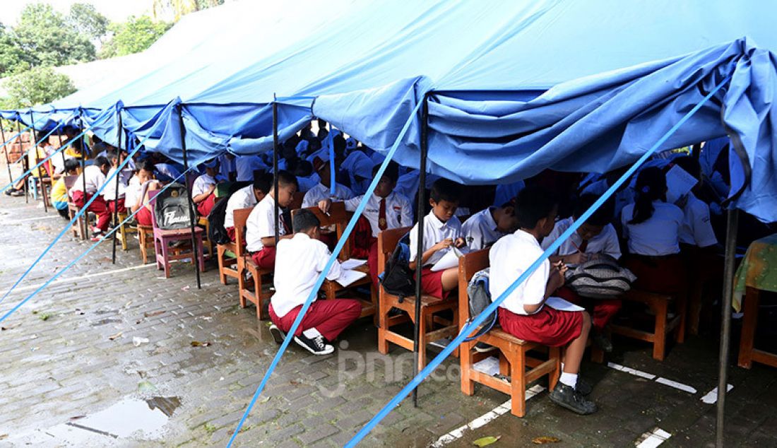 Siswa gabungan kelas 4, 5 dan 6 belajar dalam tenda darurat akibat bangunan atap kelas roboh saat hujan deras di SDN Cirimekar 2, cibinong, Bogor, Selasa (6/1). Selain ditenda darurat mereka juga belajar di lorong kelas. - JPNN.com