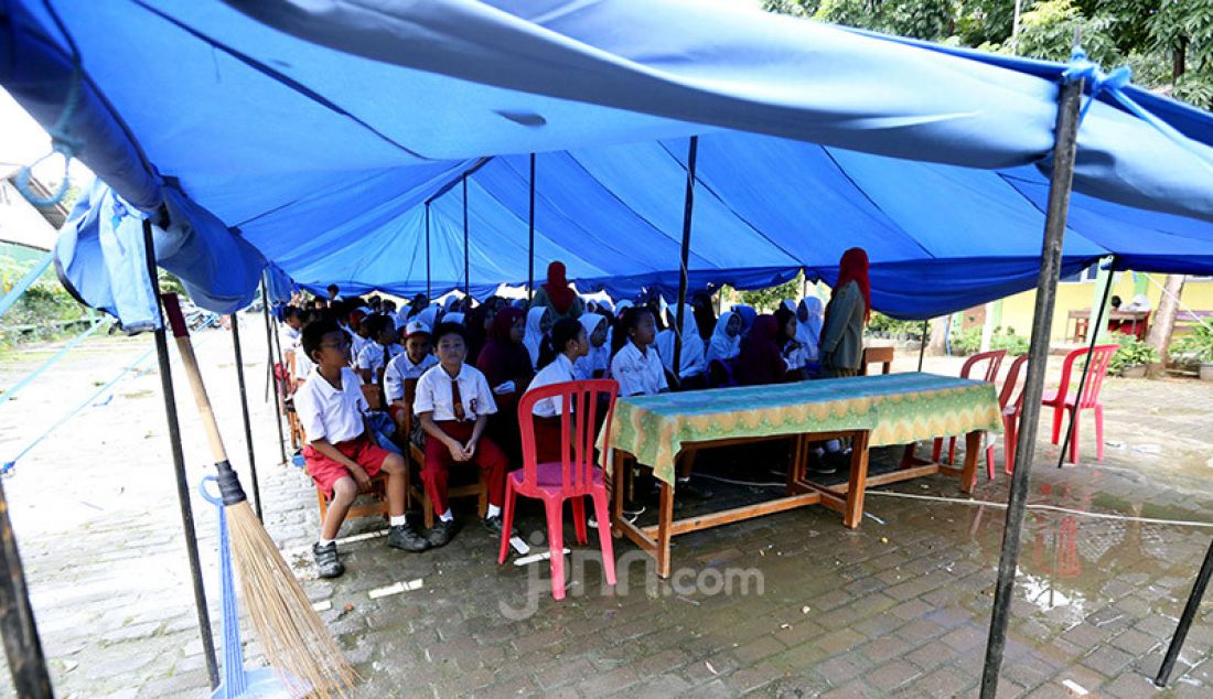 Siswa gabungan kelas 4, 5 dan 6 belajar dalam tenda darurat akibat bangunan atap kelas roboh saat hujan deras di SDN Cirimekar 2, cibinong, Bogor, Selasa (6/1). Selain ditenda darurat mereka juga belajar di lorong kelas. - JPNN.com