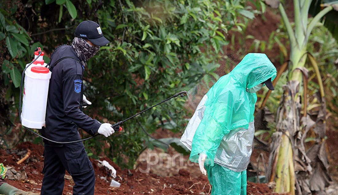 Petugas menyemprotkan cairan disinfektan kepada petugas makam usai memakamkan jenazah korban Covid-19 yang dimakamkan di TPU Pondok Ranggon, Cipayung, Jakarta Timur, Rabu (1/4). - JPNN.com