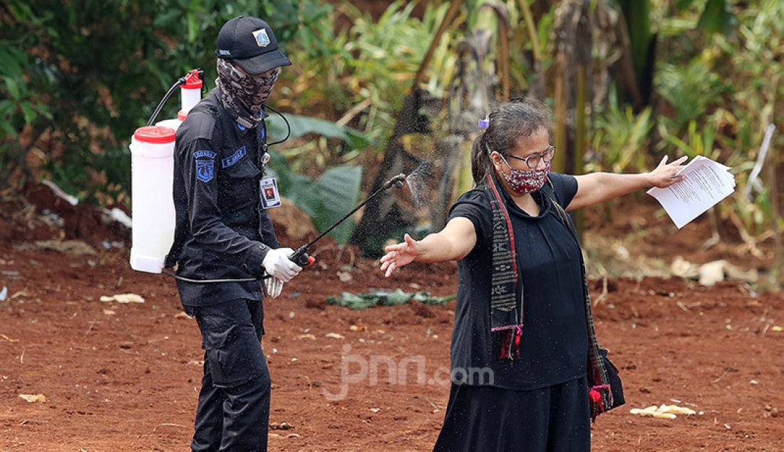 Petugas menyemprotkan cairan disinfektan kepada peziarah usai menghadiri pemakaman jenazah korban Covid-19 di TPU Pondok Ranggon, Cipayung, Jakarta Timur, Rabu (1/4). - JPNN.com