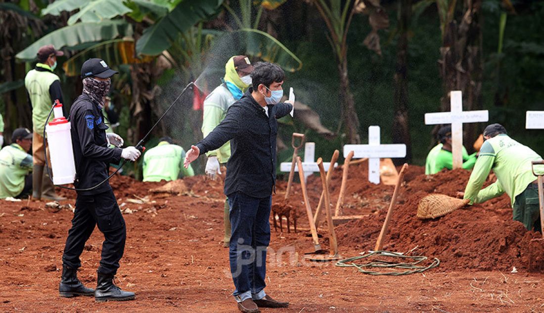 Petugas menyemprotkan cairan disinfektan kepada peziarah usai menghadiri pemakaman jenazah korban Covid-19 di TPU Pondok Ranggon, Cipayung, Jakarta Timur, Rabu (1/4). - JPNN.com