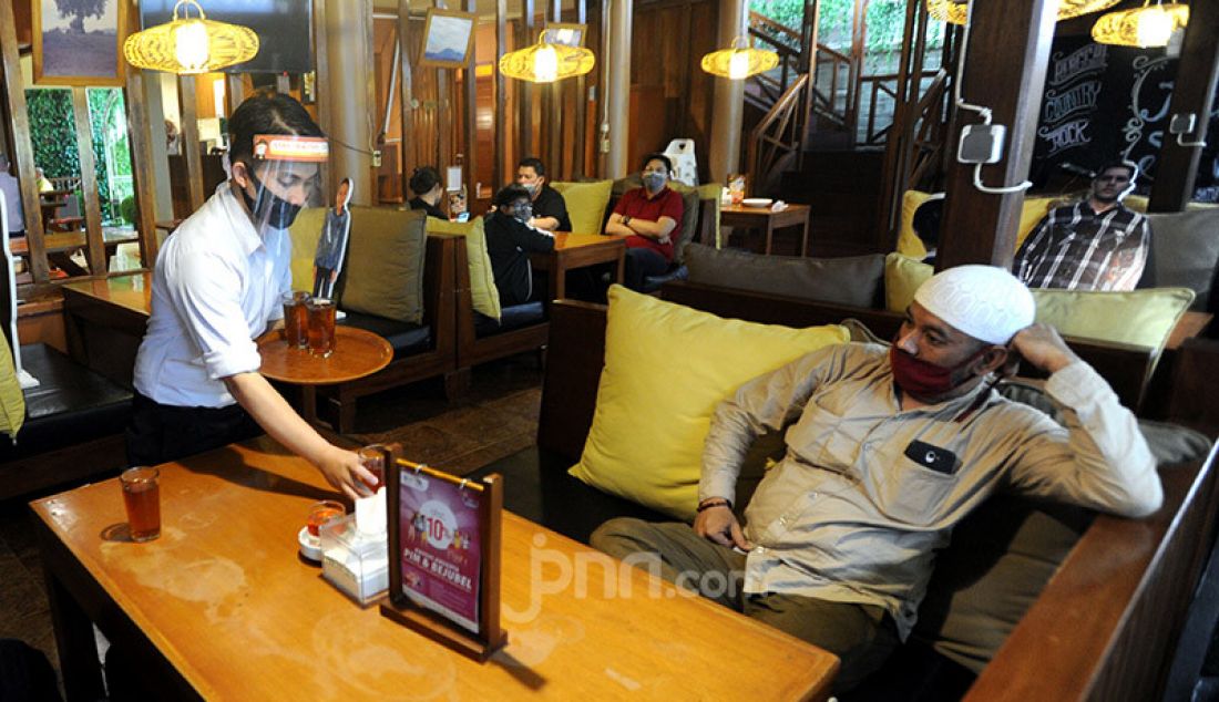 Pramusaji menggunakan alat pelindung diri wajah, masker dan sarung tangan di Rumah Makan Bumi Aki, Bogor, Senin (1/6). Penerapan protokol kesehatan ketat mulai dilakukan restoran dan rumah makan di Bogor. - JPNN.com