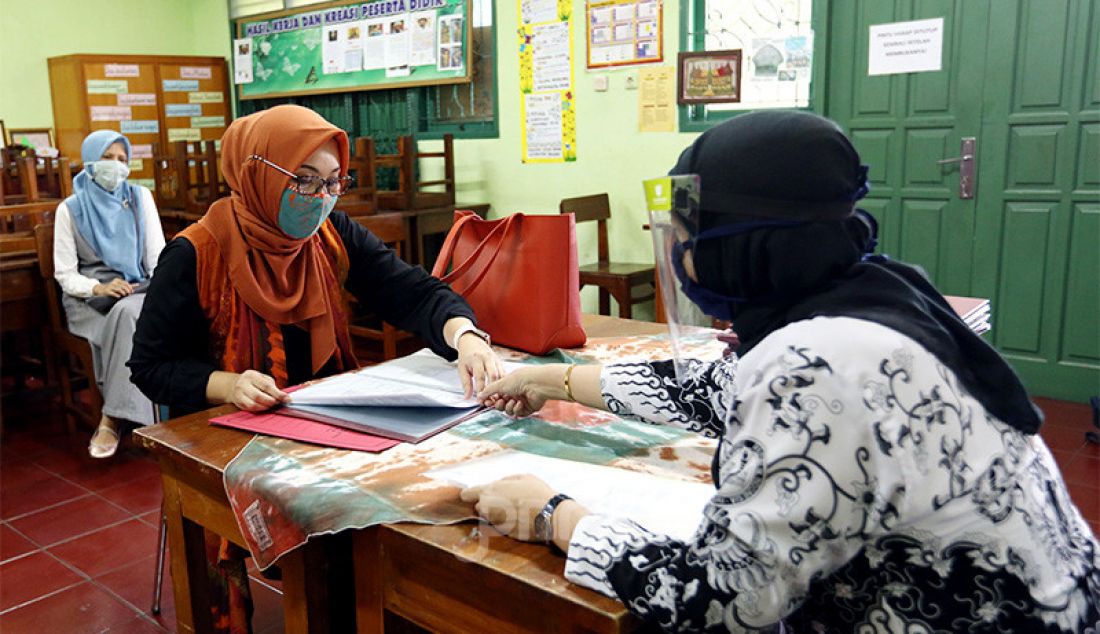 Guru membagikan laporan hasil belajar (rapor) kenaikan kelas kepada wali murid di SD Negeri Menteng 01, Jakarta, Kamis (25/6). Pembagian rapor dilaksanakan secara bertahap dari tanggal 24-26 Juni 2020, dengan mengikuti protokol kesehatan pencegahan penularan COVID-19. - JPNN.com