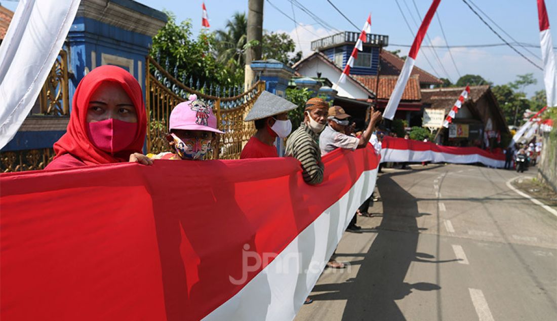 Sejumlah warga membentangkan bendera merah putih sepanjang 200 meter di Desa Cihideung Udik, Ciampea, Kabupaten Bogor, Senin (17/8). Acara tersebut dalam rangka memeriahkan peringatan HUT ke-75 Kemerdekaan Republik Indonesia. - JPNN.com