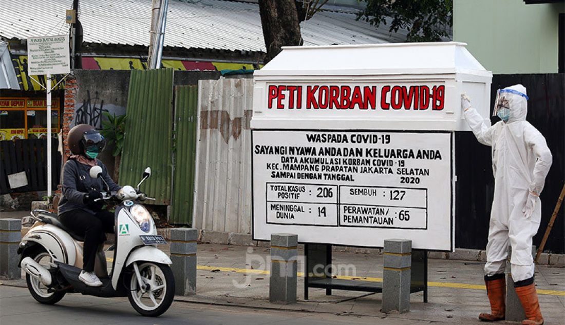 Warga melintas di samping replika peti mati disertai petugas yang menggunakan APD di kawasan Kemang, Jakarta, Selasa (18/8). Penggunaan peti mati ini dilakukan agar masyarakat sadar akan bahaya COVID-19, sehingga mematuhi protokol kesehatan. - JPNN.com