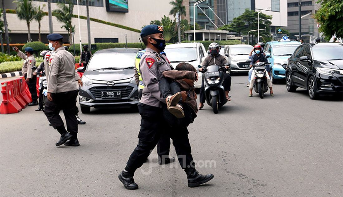 Petugas kepolisian mengangkat seorang pelajar terpaksa yang terjaring razia di kawasan Bundaran HI, Jakarta Pusat, Selasa (13/10). Polisi melakukan razia dalam rangka pengamanan unjuk rasa memprotes Omnibus Law Cipta Kerja di kawasan Patung Kuda, Kebon Sirih. - JPNN.com