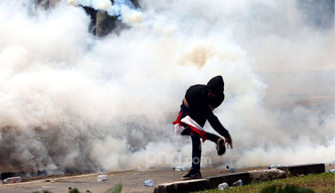 Seorang pengunjuk rasa melemparkan gas air mata yang ditembakkan petugas ke arah kerumunan demonstran di kawasan Patung Kuda, Kebun Sirih, Jakarta Pusat, Selasa (13/10). - JPNN.com